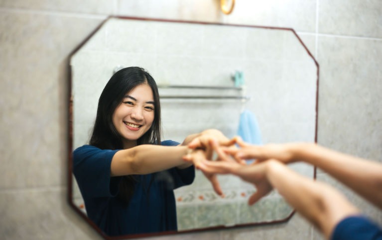Woman looking and reaching out her arms to a mirror smiling